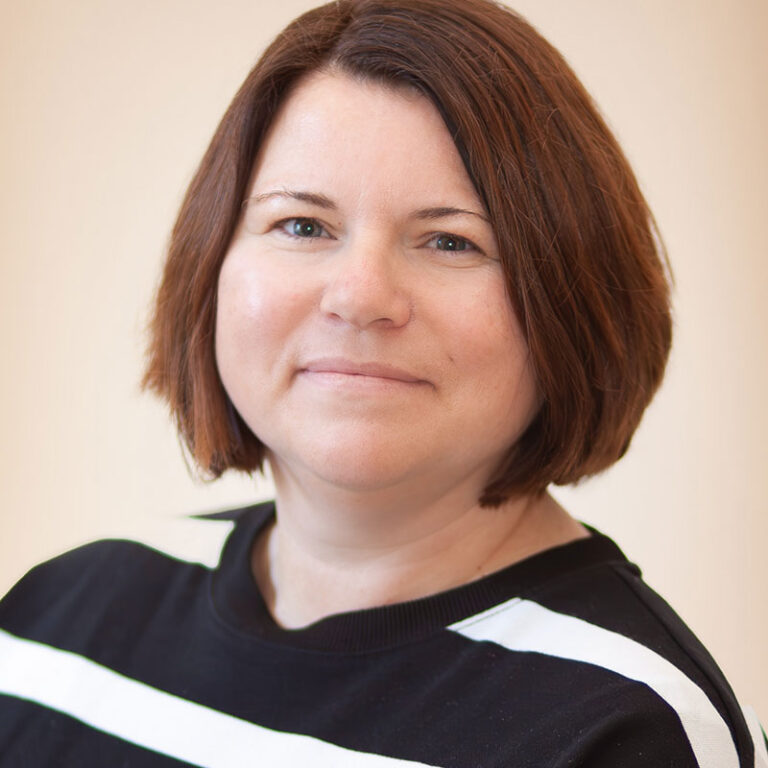 Portrait von Sabrina Backenköhler, Mitarbeiterin der Stiftung Heilpädagogisches Kinderhaus Stemwede. Sie hat kurze, glatte braune Haare in einem kinnlangen Bob und einen ruhigen, freundlichen Gesichtsausdruck. Sie blickt direkt in die Kamera. Sie trägt ein schwarzes Oberteil mit weißen Streifen an den Schultern. Der Hintergrund ist hell und neutral.